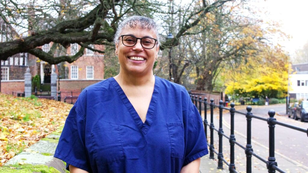 Mixed race healthcare support worker in scrubs smiling under a tree